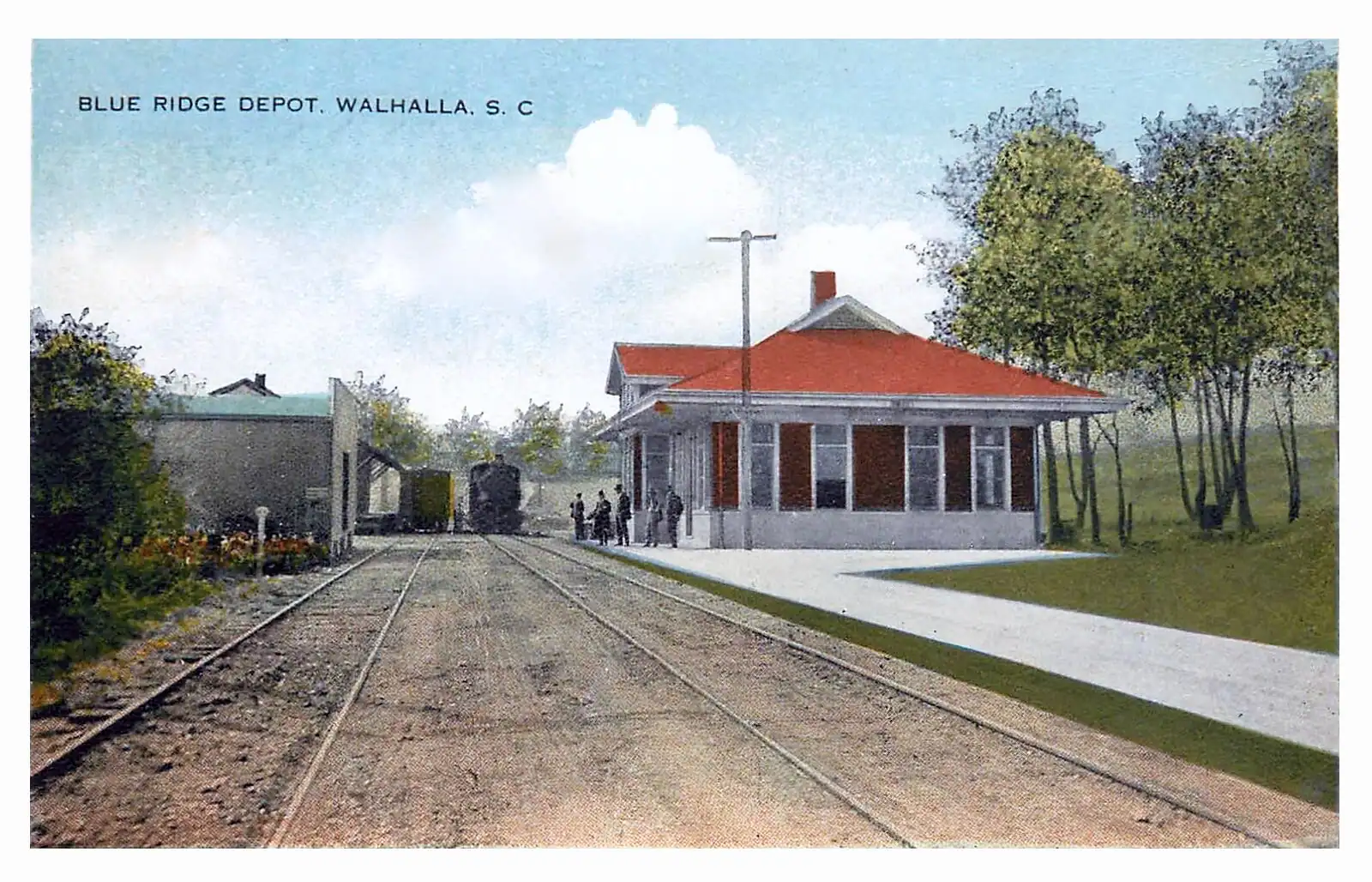 A railway depot with locomotives standing on the tracks below a forested hill