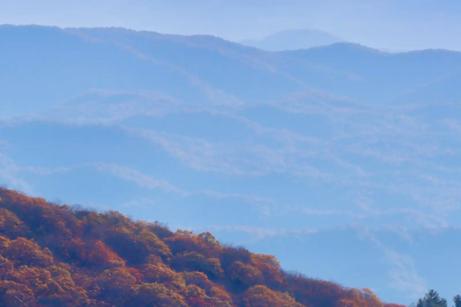 Layered blue ridgelines fading into haze with autumn colour across the nearest slopes